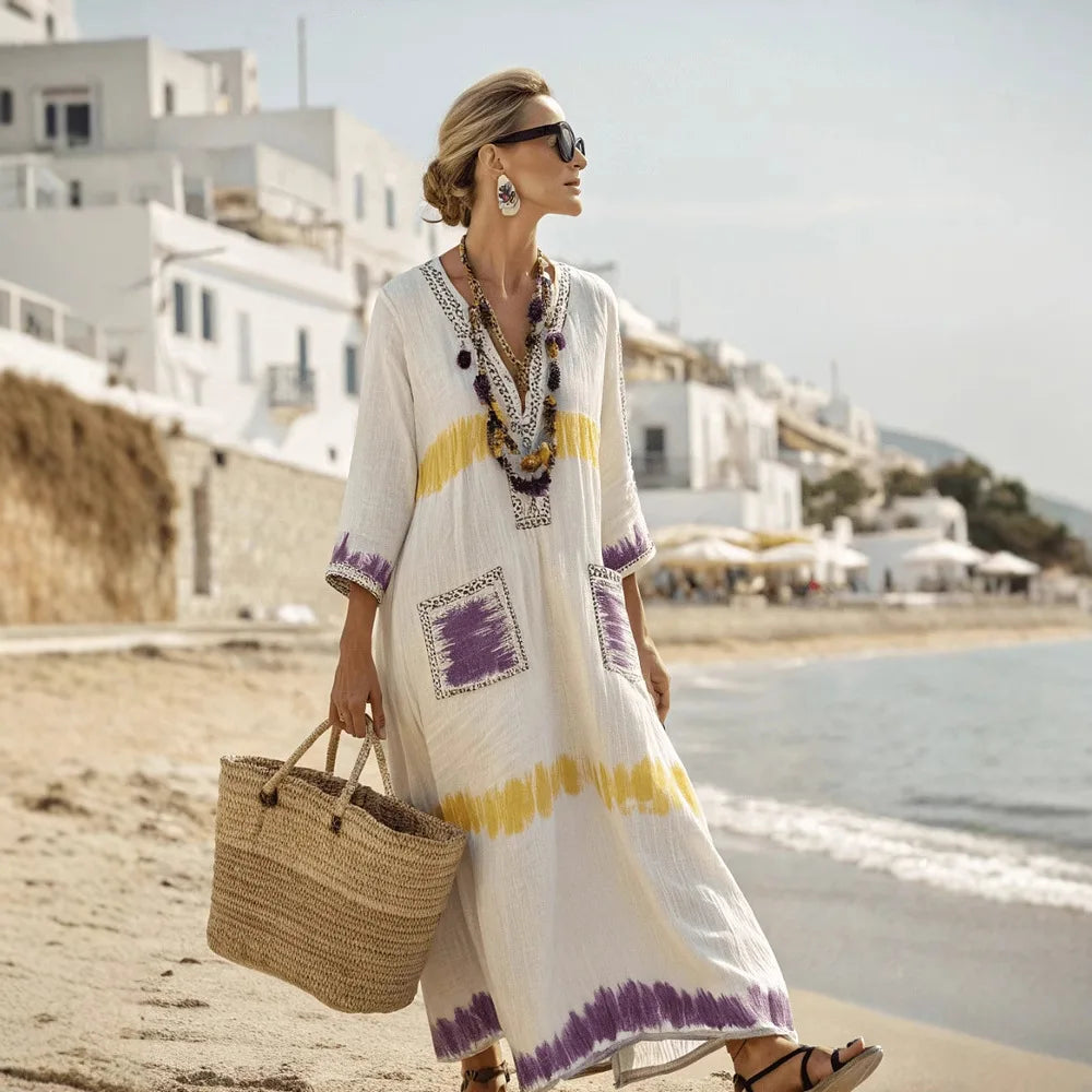 Woman in a long, patterned dress on a beach with a scenic background
