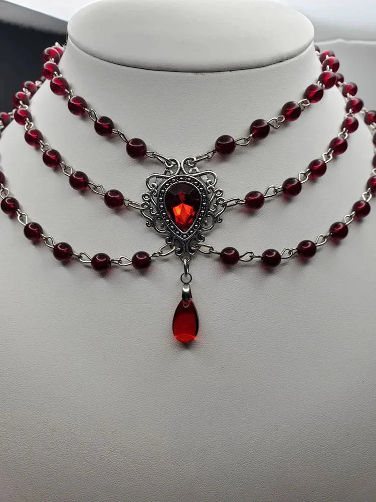Three-strand gothic necklace with dark red beads, ornate red gemstone centerpiece, dangling drop