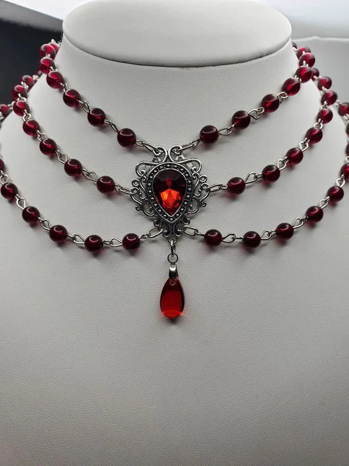 Three-strand gothic necklace with dark red beads, ornate red gemstone centerpiece, dangling drop