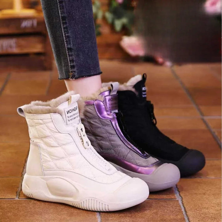 Three pairs of winter boots in white, purple, and black on a tiled floor.