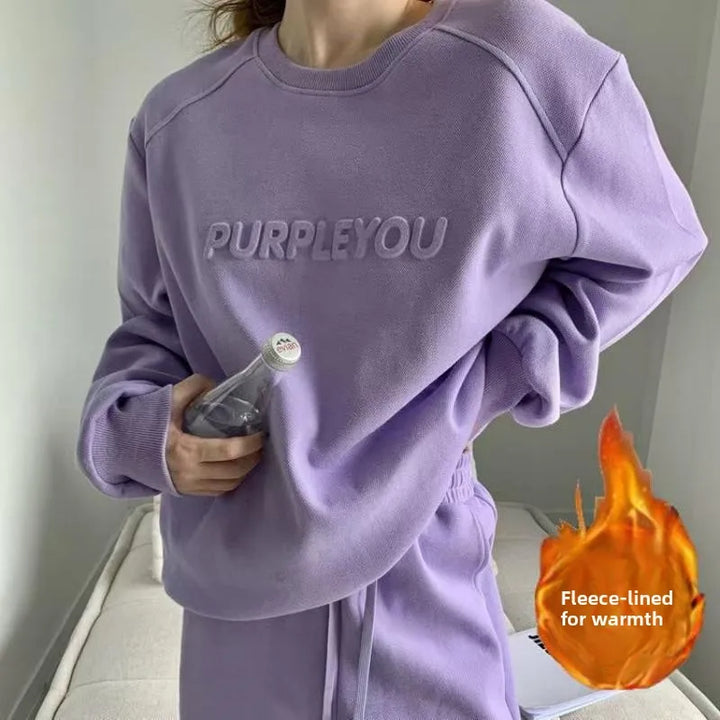 A person wearing a lavender-purple fleece sweatshirt with 'PURPLEYOU' printed across the chest, holding a glass bottle. The image includes a flame graphic and the text 'Fleece-lined for warmth' as an overlay.