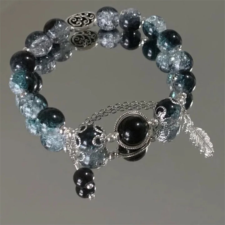 Bead charm bracelet with teal and dark beads, round center charm, and feather dangle