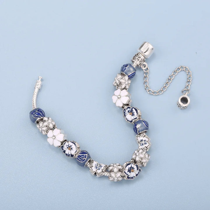 Silver charm bracelet with blue bead segments and white flower charms, shown laid out