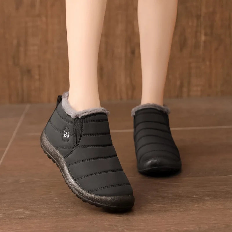 Black winter boots with gray lining worn indoors on a wooden floor.