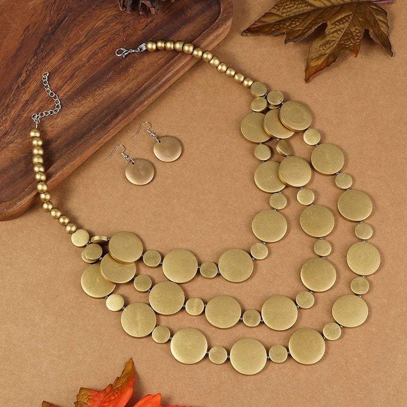 Gold-tone disc beaded necklace with round dangle earrings laid out on a surface
