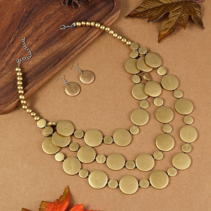 Gold-tone disc beaded necklace with round dangle earrings laid out on a surface