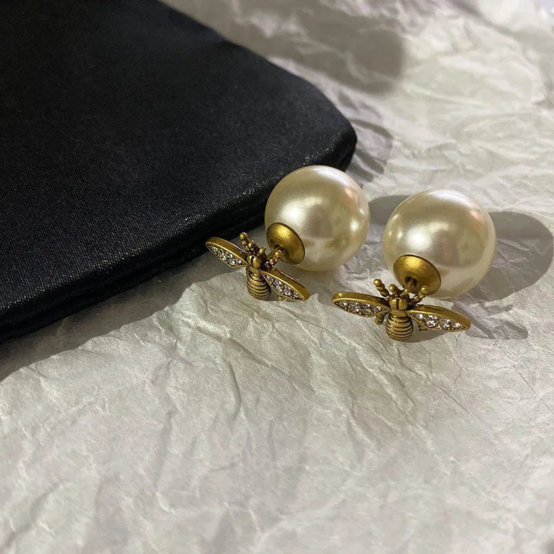 Pearl earrings with bee-like designs on a textured surface