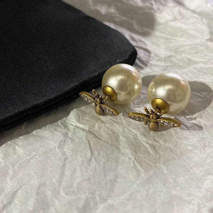Pearl earrings with bee-like designs on a textured surface