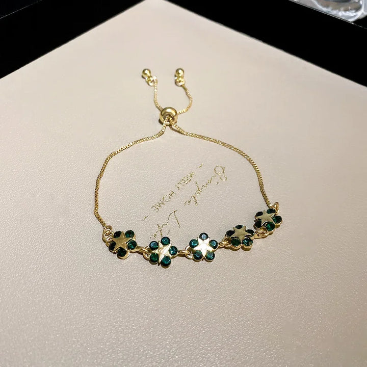Gold-tone charm bracelet with green clover motifs on a delicate chain