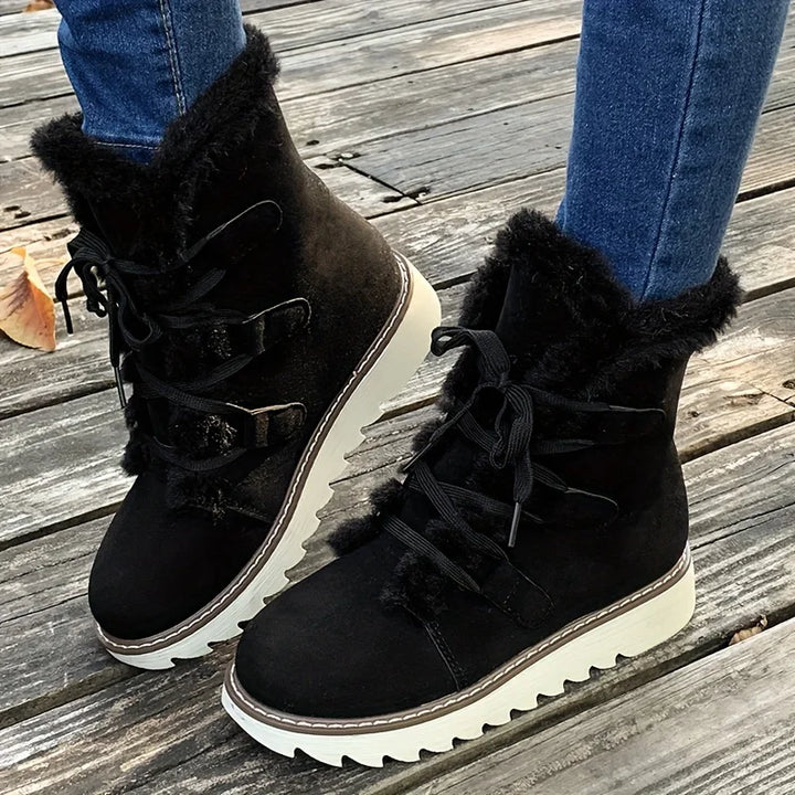 Black suede boots with fur trim worn on a wooden floor