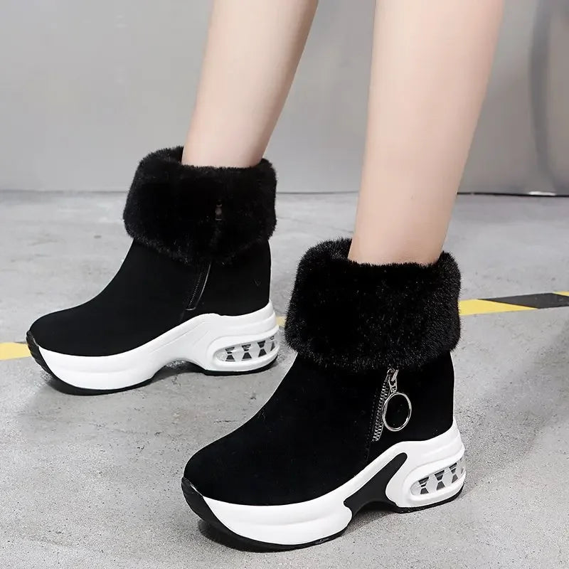 Black winter boots with white soles and fur trim on a gray floor.