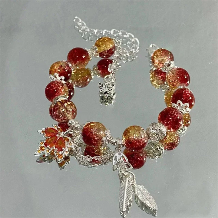 Charm bead bracelet with red, gold, and clear beads, butterfly charm, and leaf dangles