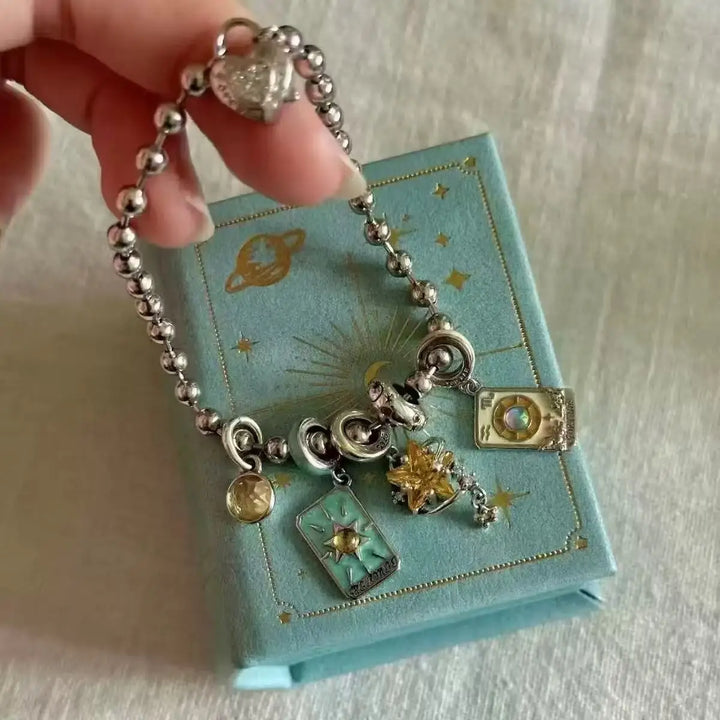 Silver charm bracelet held over a blue jewelry box with star patterns.