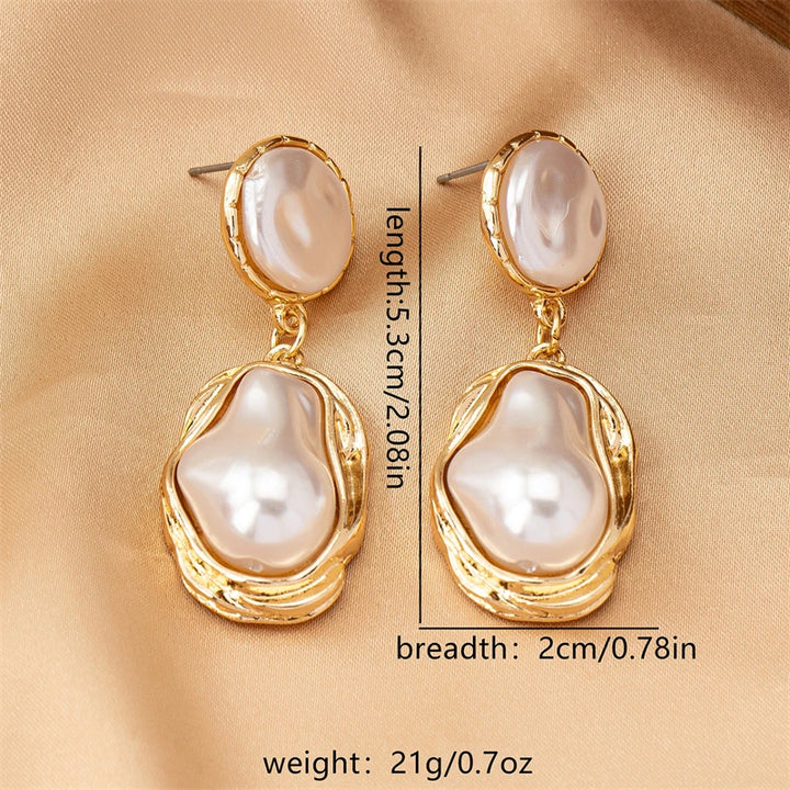 Pearl earrings with gold accents on a beige fabric background, showing measurements.