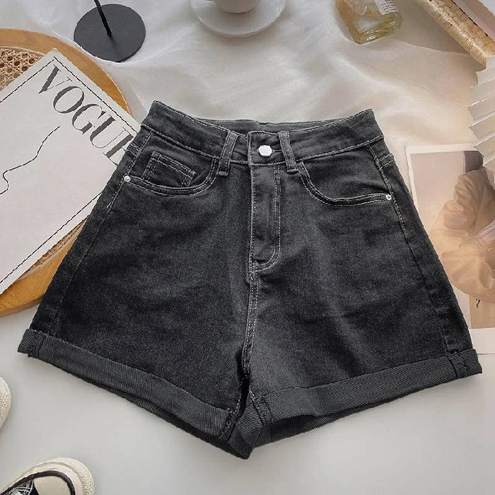 Black denim shorts on a light surface with a magazine and coffee cup in the background