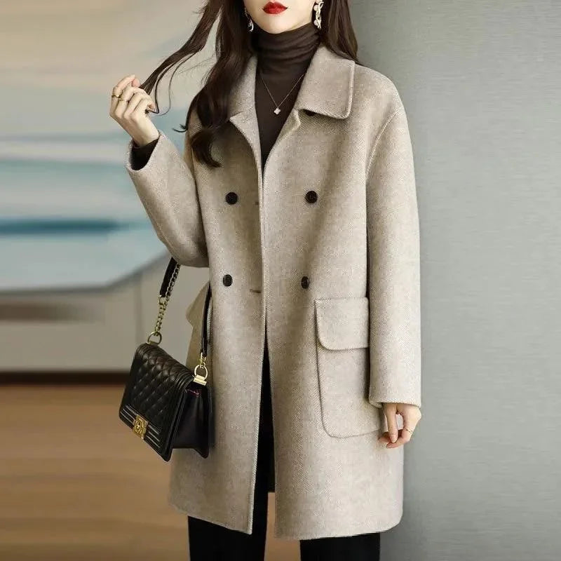 Woman wearing a beige coat holding a black handbag against a neutral background