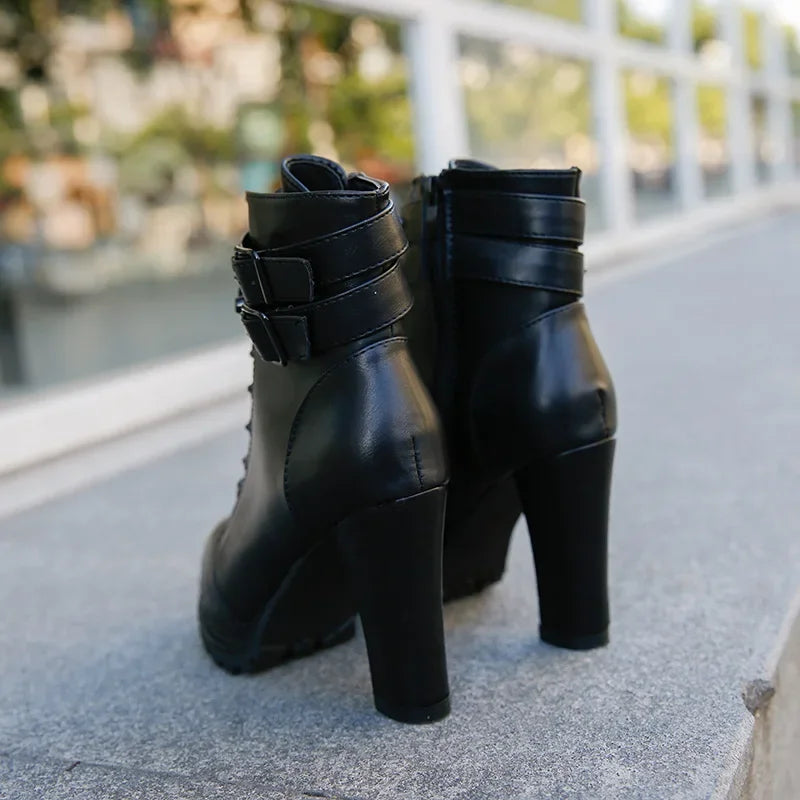 Black high-heeled boots with strap details on a concrete surface.