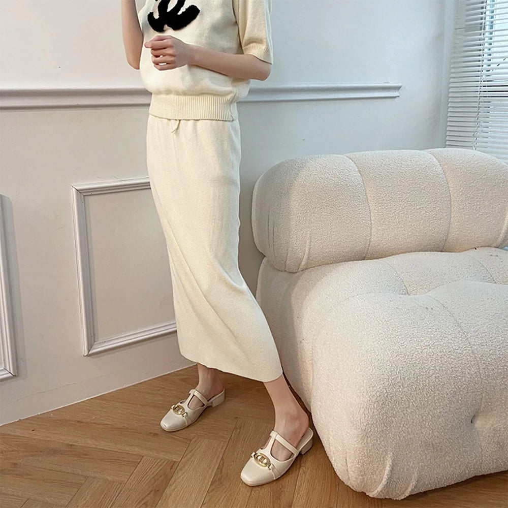 Person wearing a beige outfit standing next to a white sofa in a room with light blue walls.