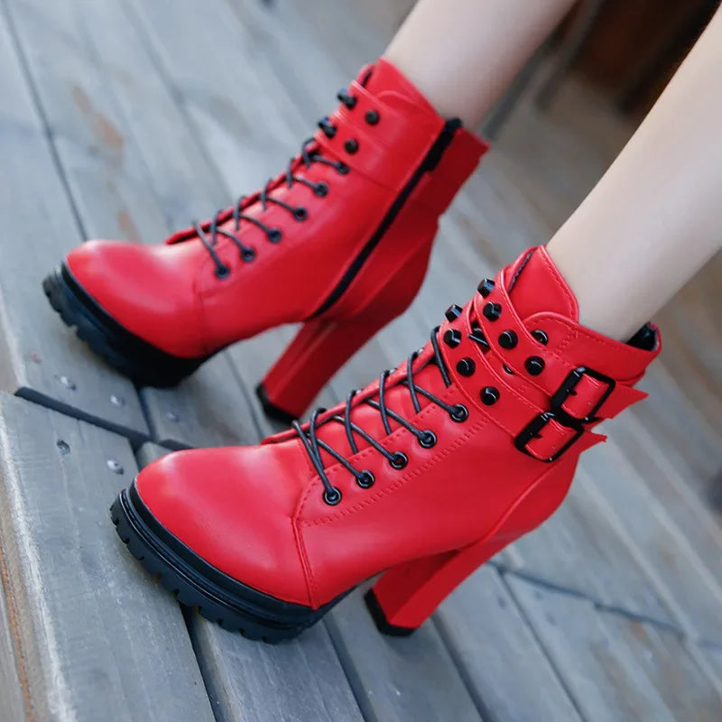 Red high-heeled boots with black laces and buckles on a wooden floor.