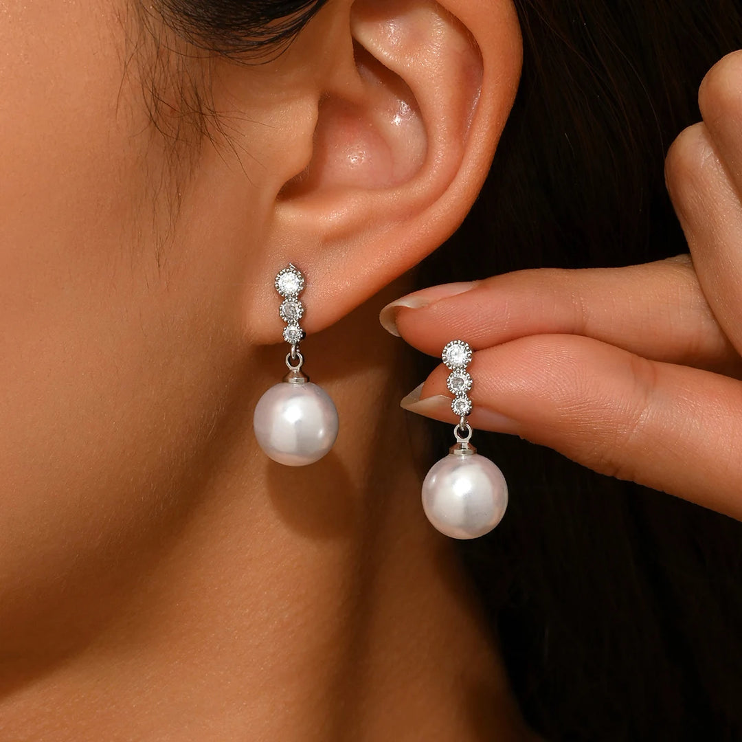 Silver-tone zircon and pearl drop dangle earrings, close-up on ear