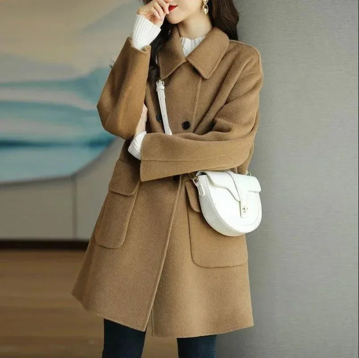 Person wearing a brown coat with a white handbag against a neutral background