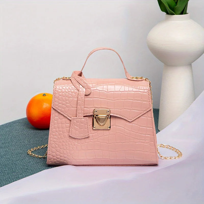 Pink handbag with gold chain on a surface with an orange and vase in the background