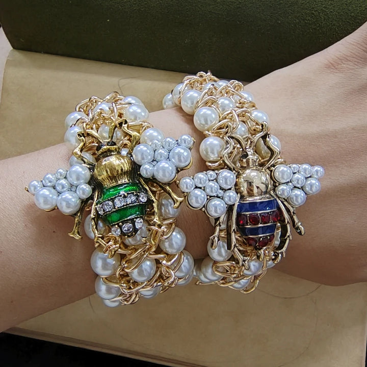 Two ornate bracelets with bee designs and pearl accents on a wrist.
