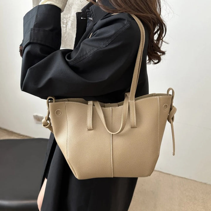 Beige handbag held by a person wearing a black coat indoors.
