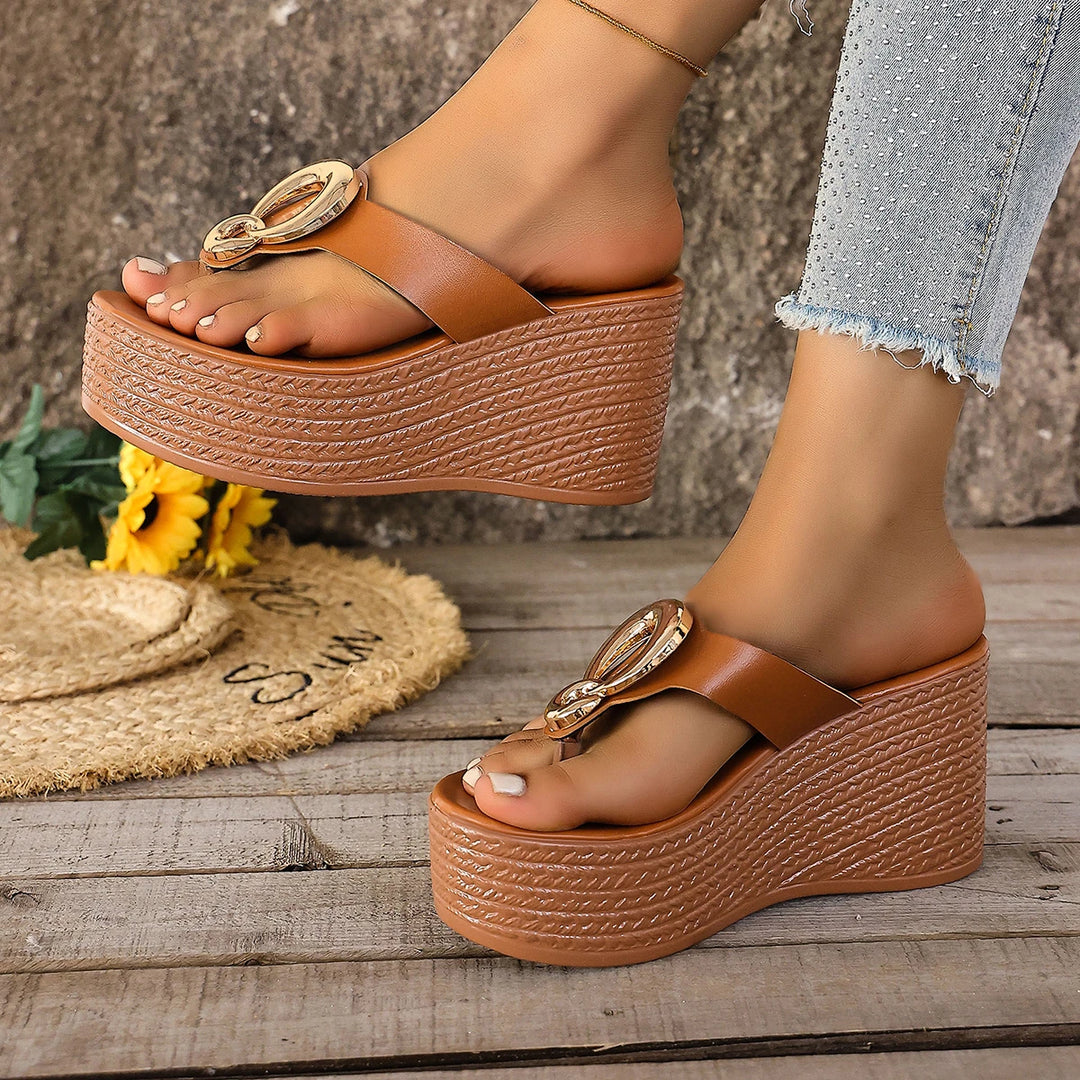 Brown platform sandals with decorative straps worn by a person on a wooden floor.