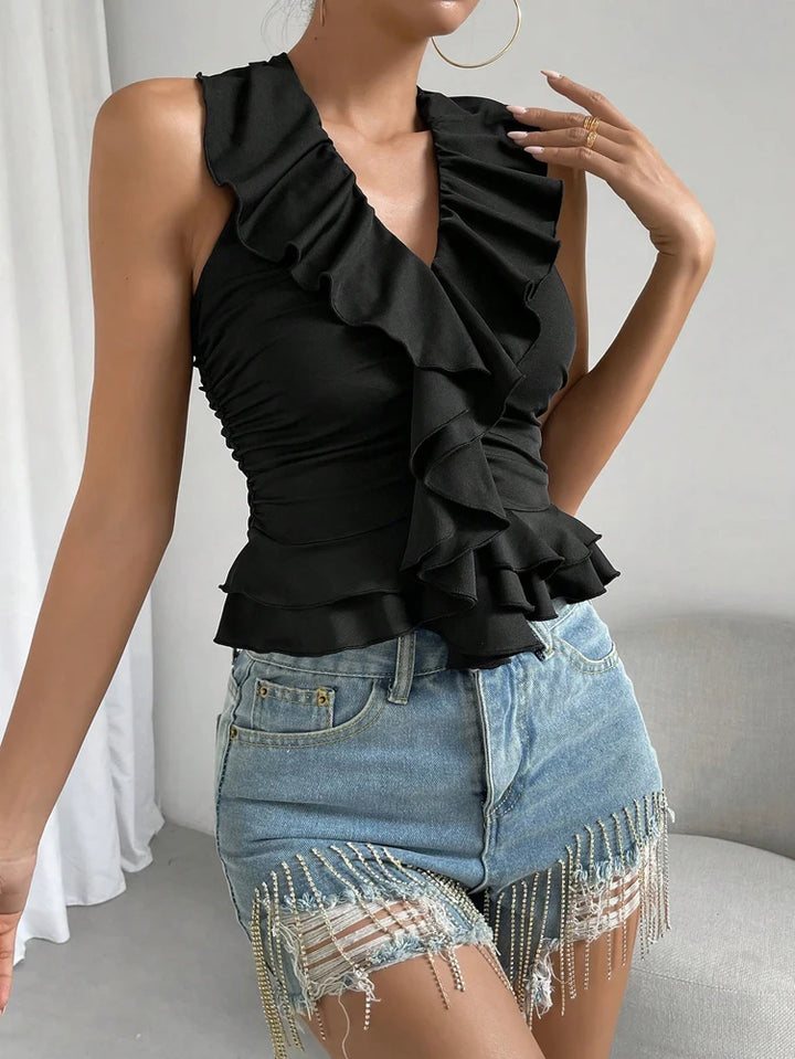 Woman wearing a black ruffled top and denim shorts with fringe details.