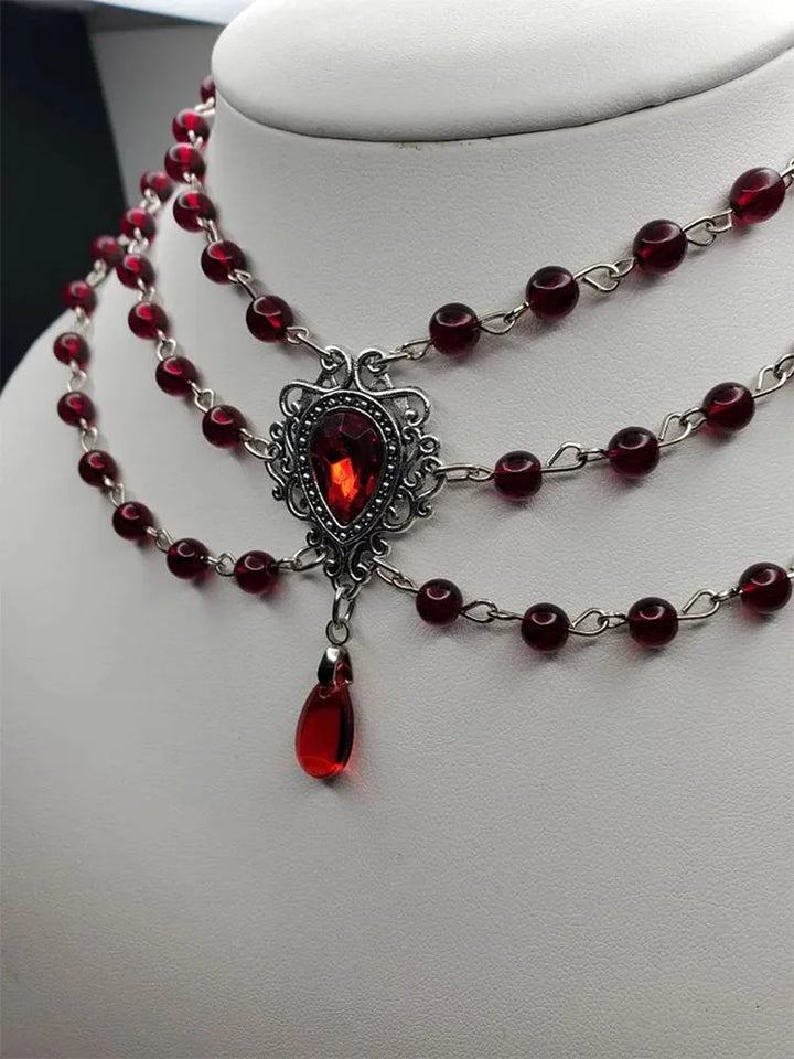 Ornate centerpiece on gothic bead necklace with dark red beads and dangling red teardrop charm