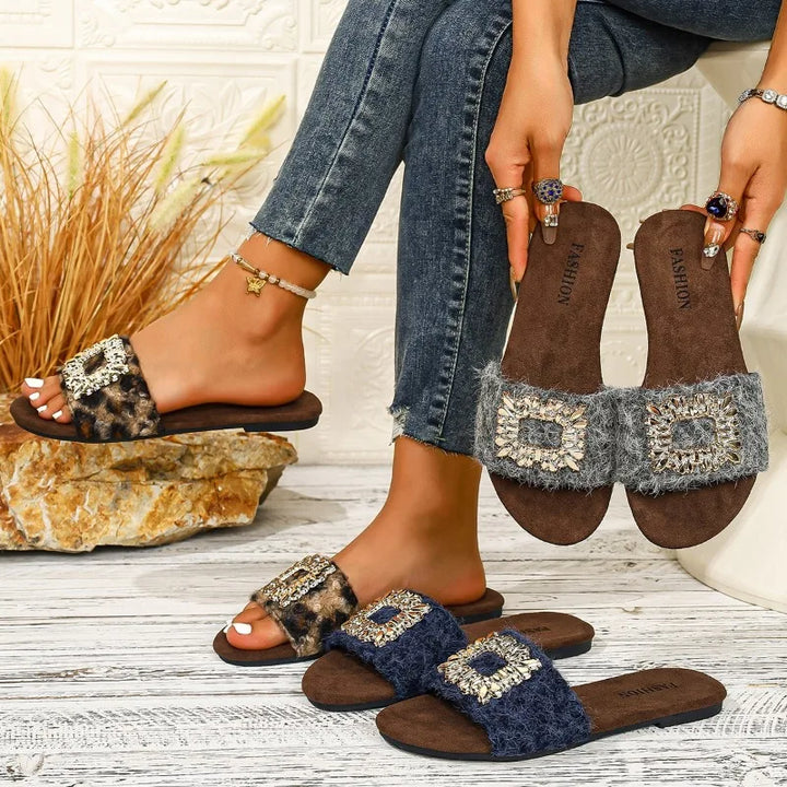 Brown sandals with decorative straps worn by a person on a wooden floor.