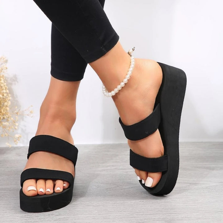 Black platform sandals worn with black leggings on a light background