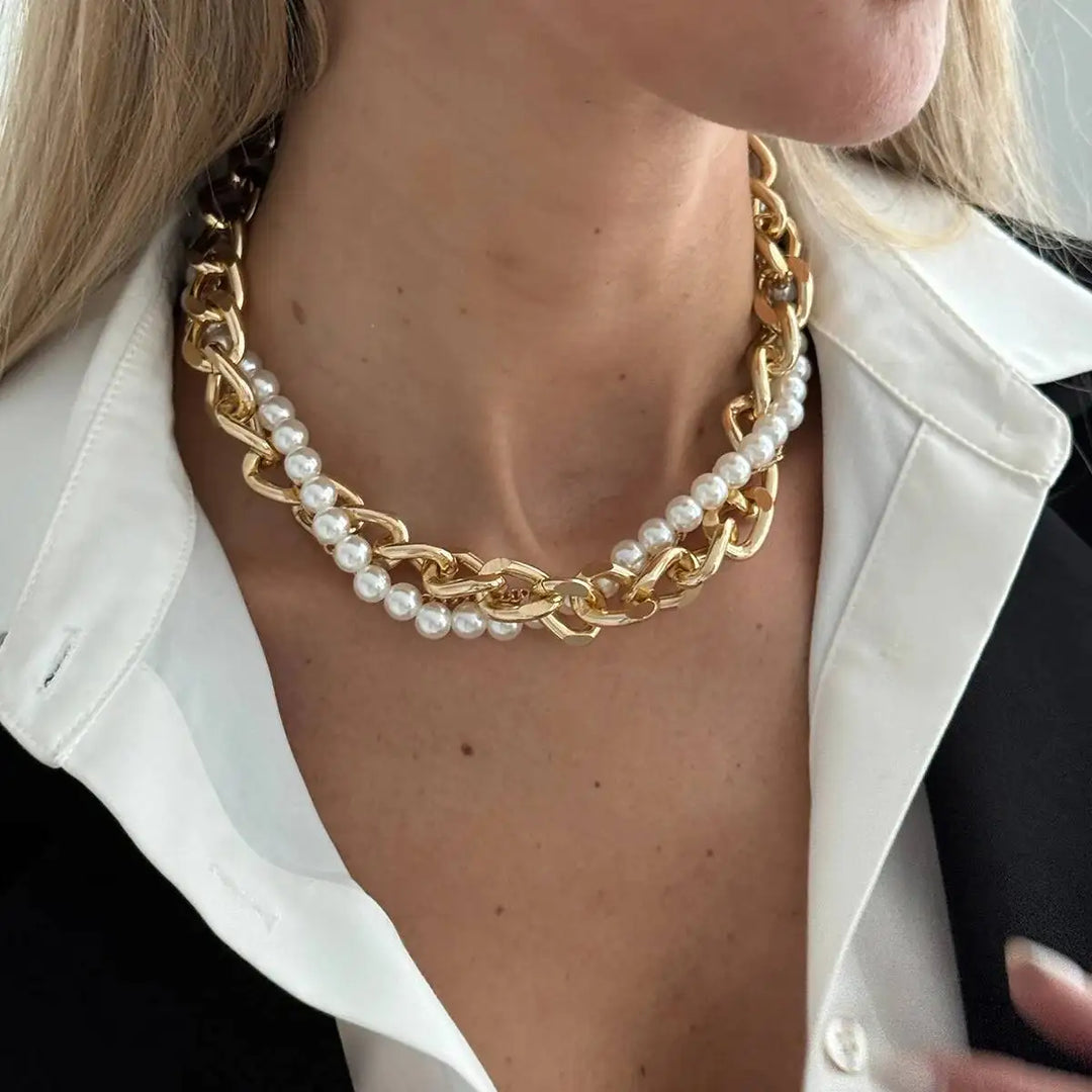 Gold chain and pearl necklace worn by a person with a white shirt.