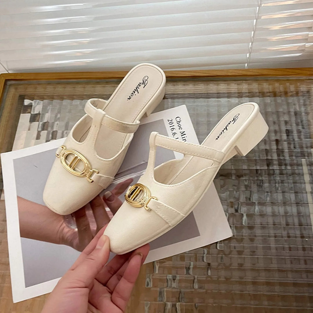 Beige shoes with gold embellishments held by a hand on a textured surface.