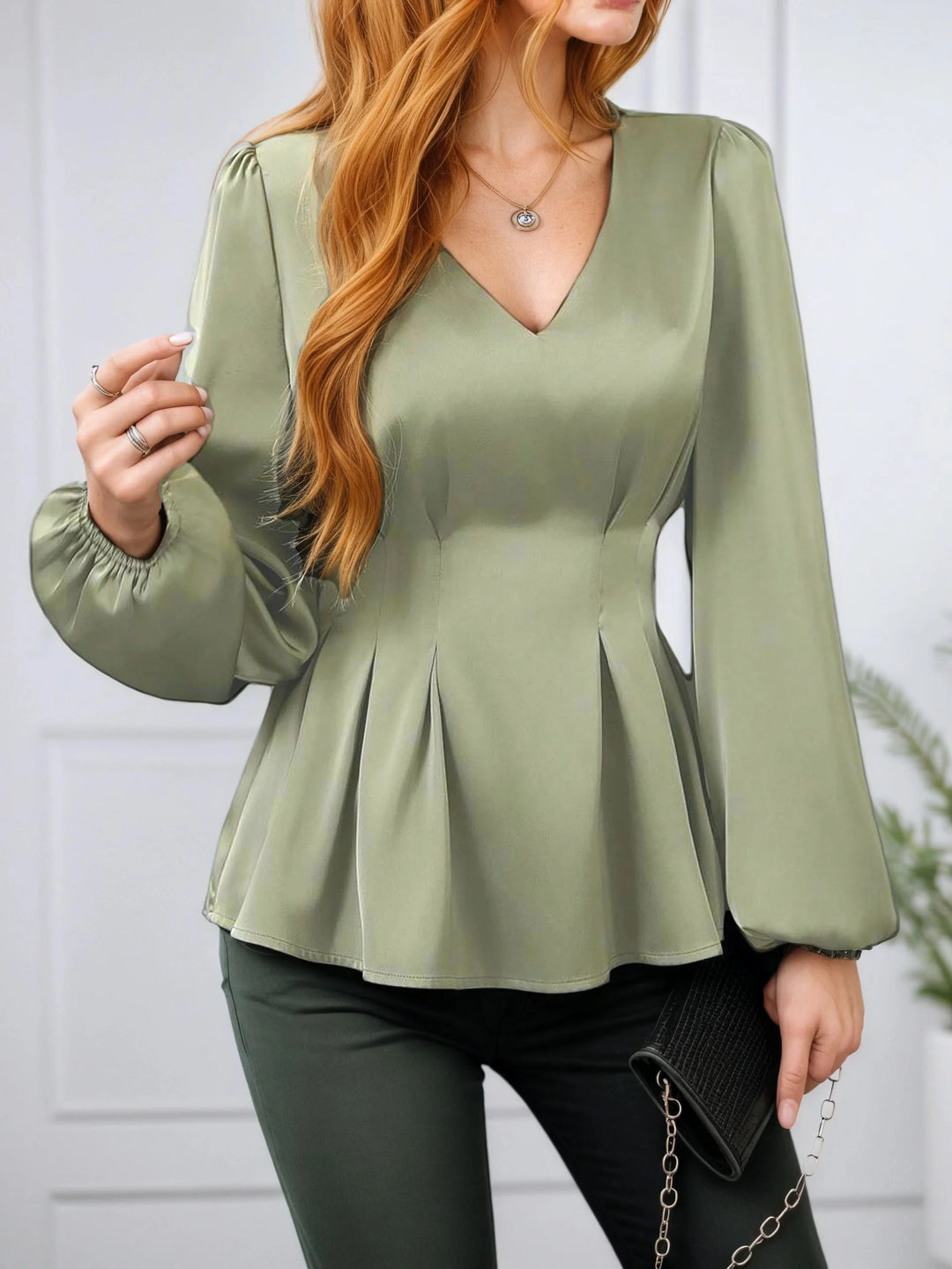 Person wearing a green peplum top with long sleeves against a white background