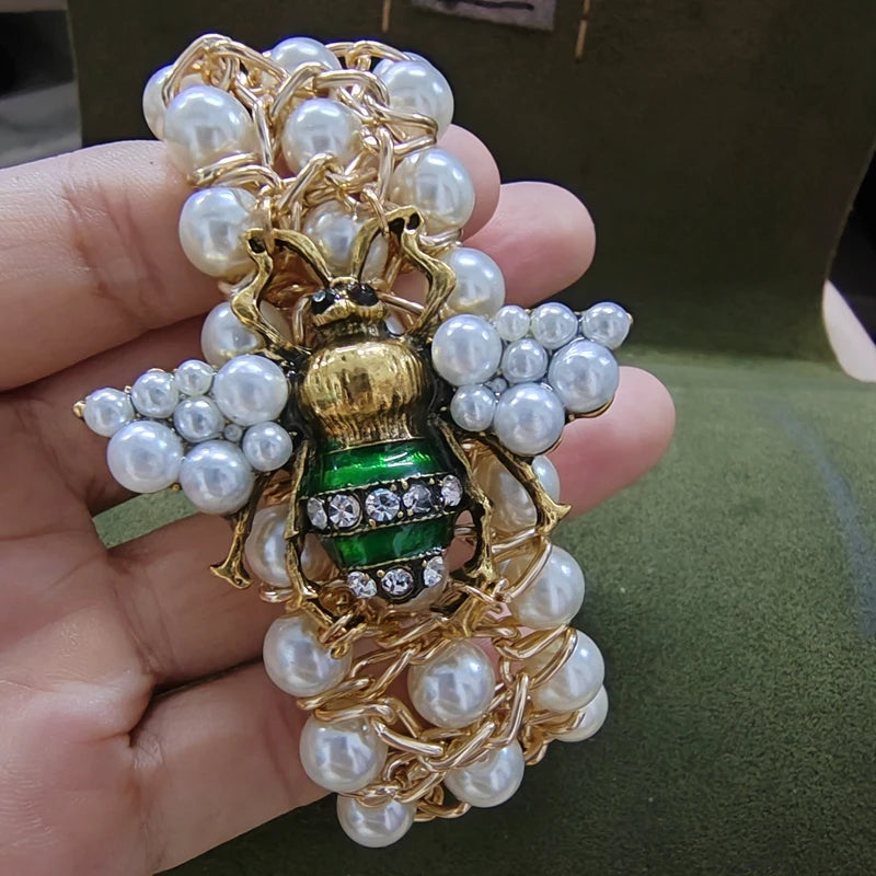 Gold and pearl brooch held in a hand with a green background