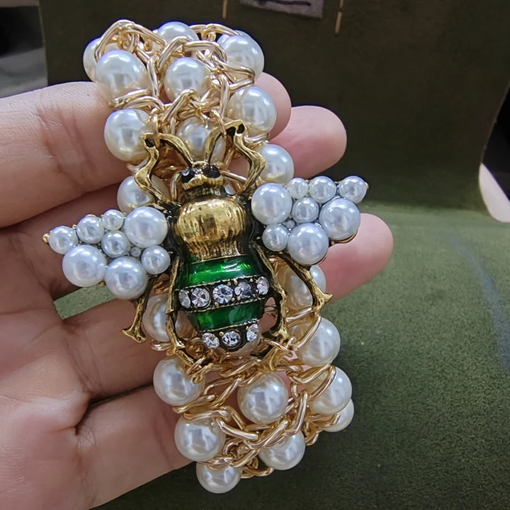 Gold and pearl brooch held in a hand with a green background