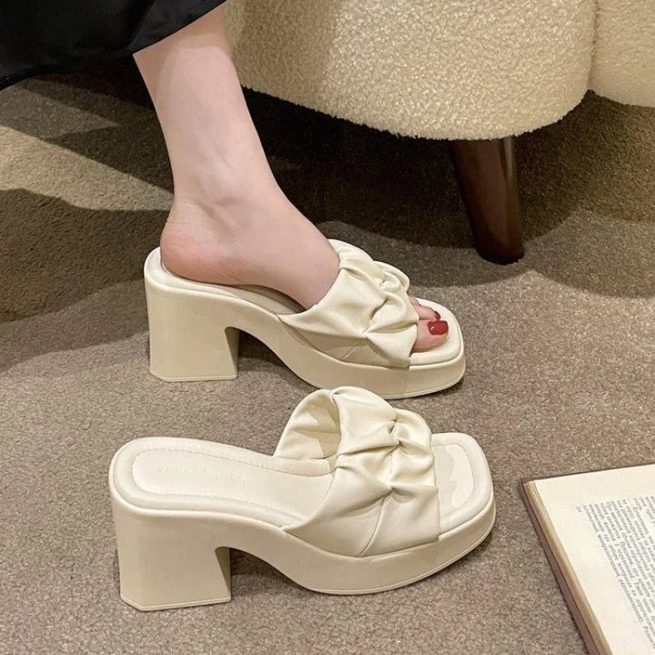 White sandals with bow details on a carpeted floor.