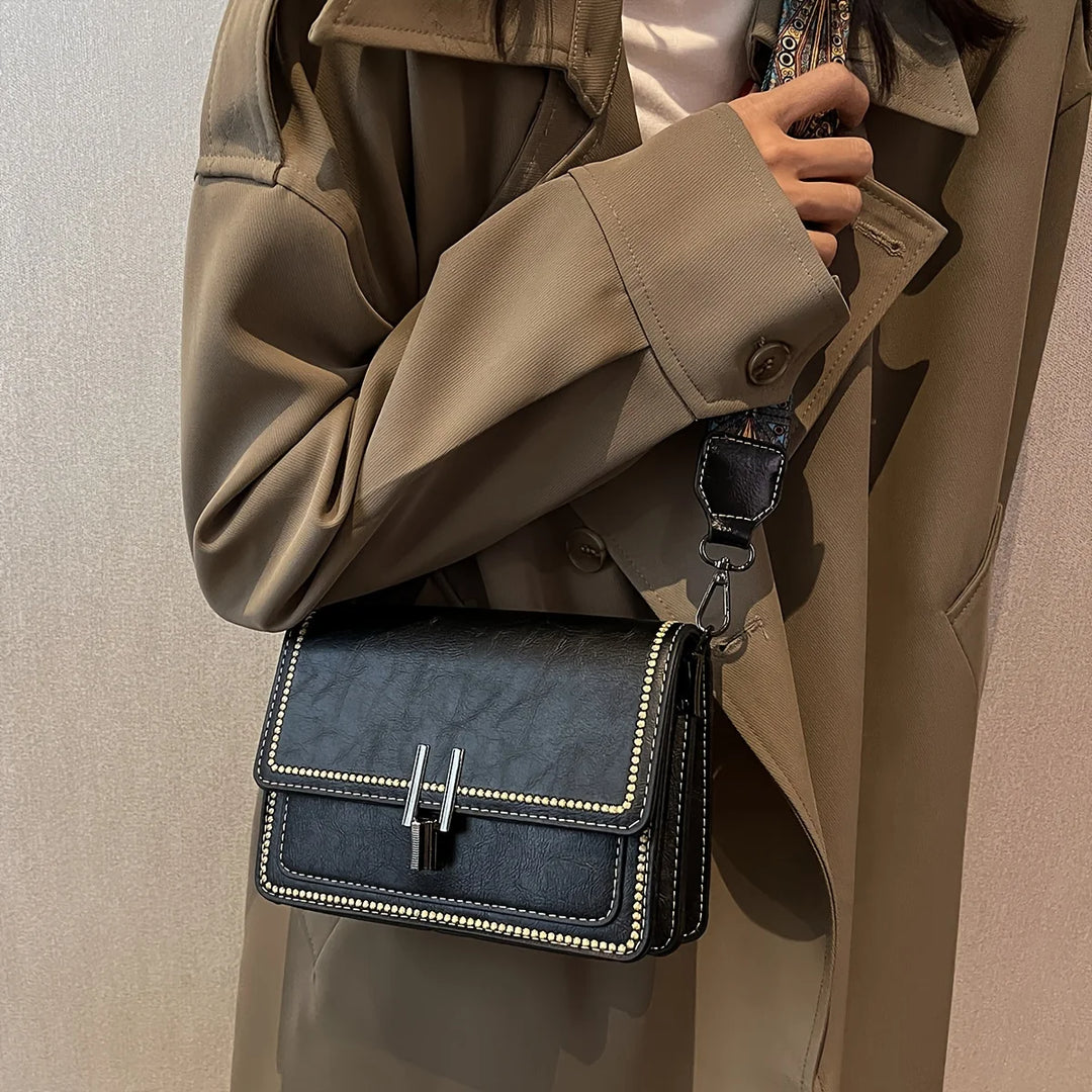 Mini crossbody bag in dark navy with flap lock, beaded trim, and patterned shoulder strap