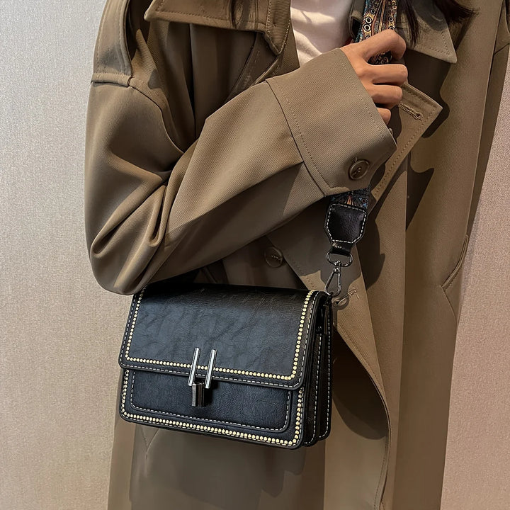 Mini crossbody bag in dark navy with flap lock, beaded trim, and patterned shoulder strap