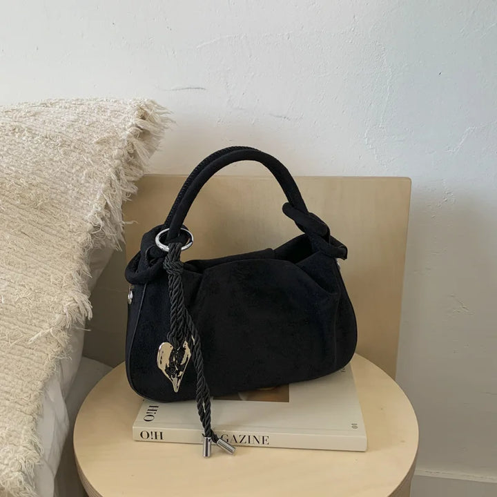 Black suede mini hobo crossbody bag with short handles, braided cord, and heart charm.