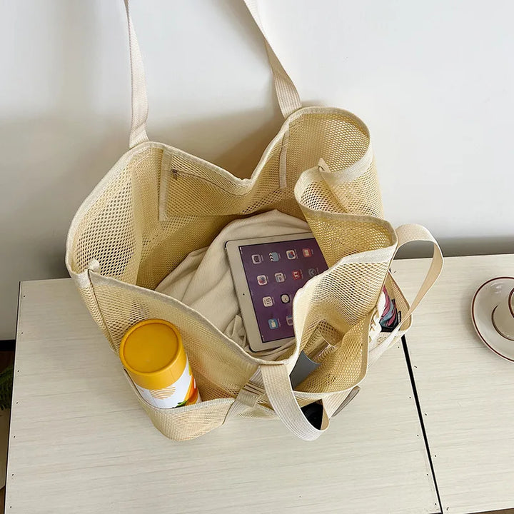 Beige sheer mesh tote bag with open top holding a tablet, bottle, and small items