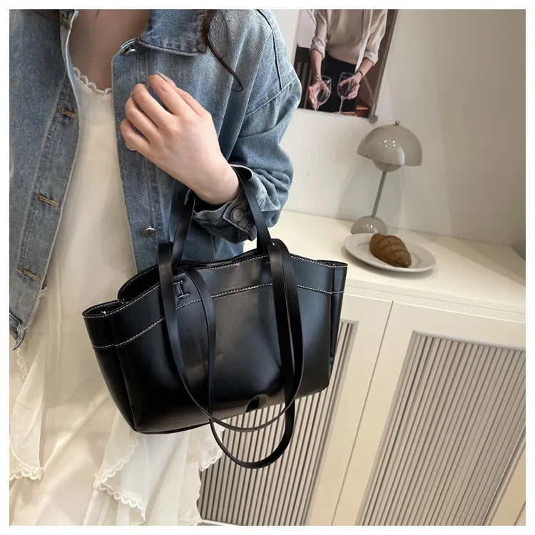 Person holding a black handbag in a room with a lamp and plate on a surface.