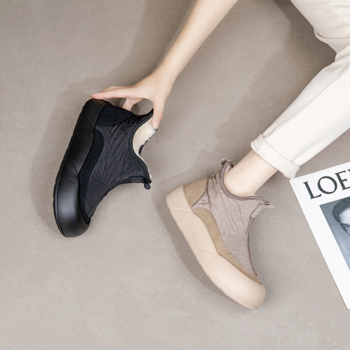Person holding a black shoe next to a beige shoe on a neutral background