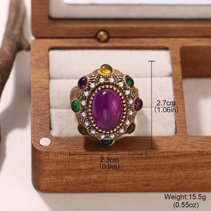 Gold oval statement ring with purple gemstone, pearl-like detailing, green and purple stones