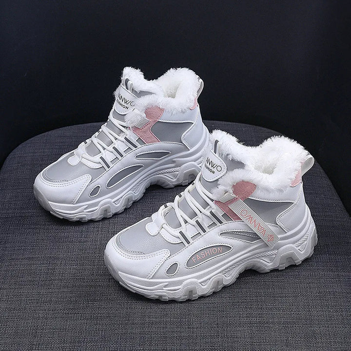 A pair of white and gray mid-height winter sneakers with white faux-fur lining and pink accents, displayed on a dark gray textured surface against a black background.