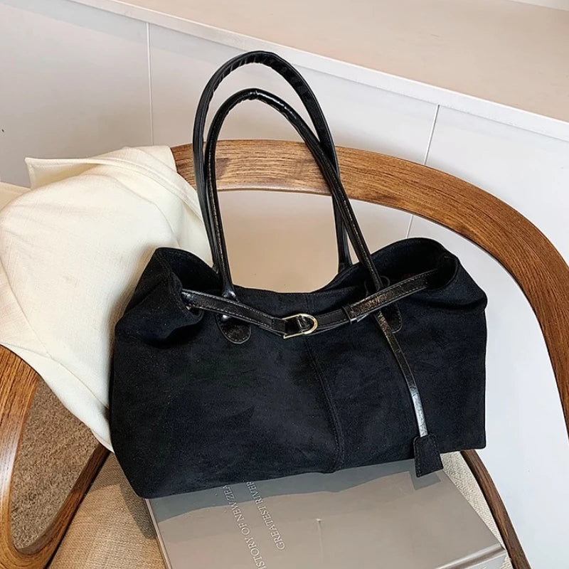 Women’s suede tote bag in black with double handles and front buckle strap.