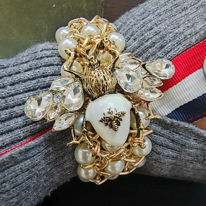 Decorative brooch with pearls, crystals, and a central heart design on a textured fabric background.