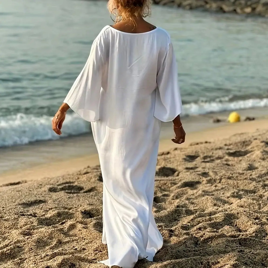 Person wearing a white dress walking on a beach with ocean in the background